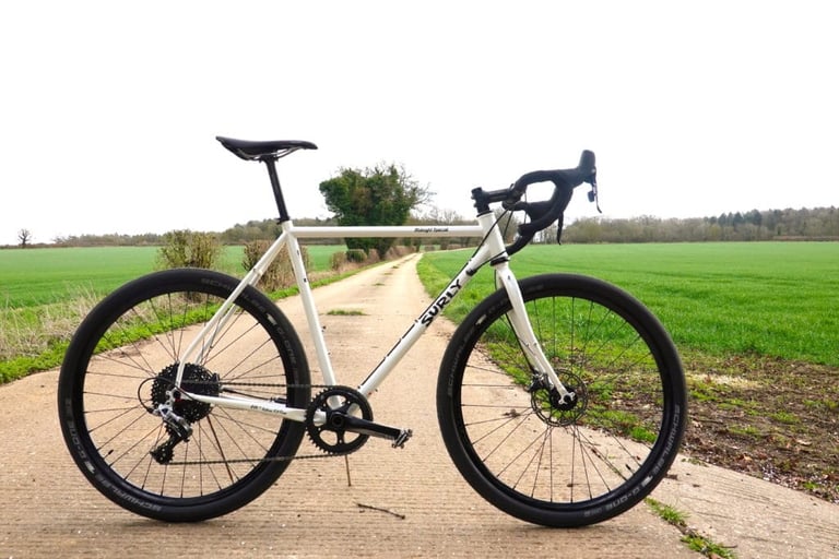 Side view of the white Surly Midnight Special 1x HRD on 650b wheels, on a track beside a field.