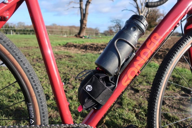 76 Projects Piggy fitted below the bottle cage on the down tube of a red Sonder Camino AL, beside a ploughed field.