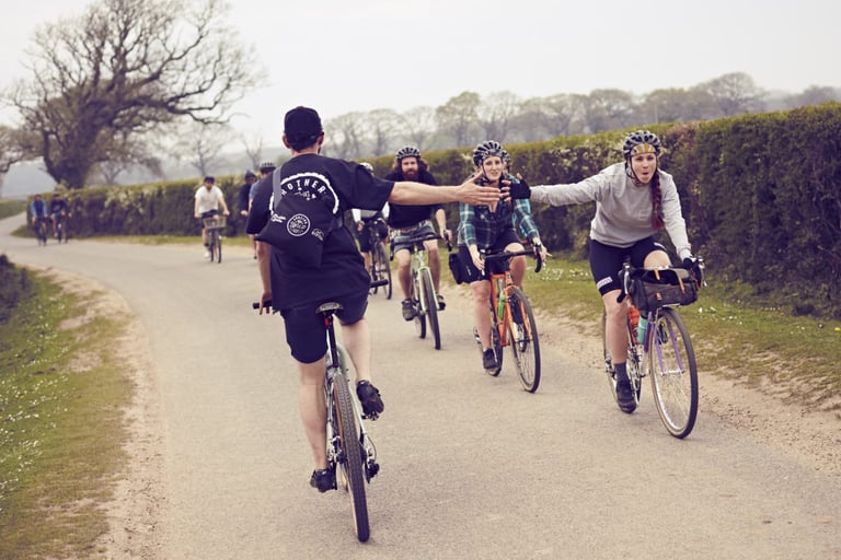 Brother in the Wild riders high-five as they pass on a country lane, one with a bar bag on a gravel bike.