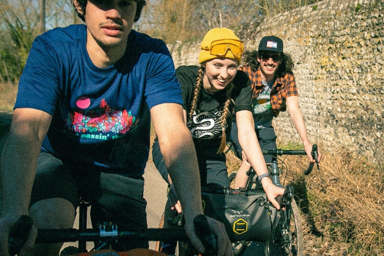 Three riders in casual Morvélo Overland kit on a country lane, one with an Apidura handlebar bag.
