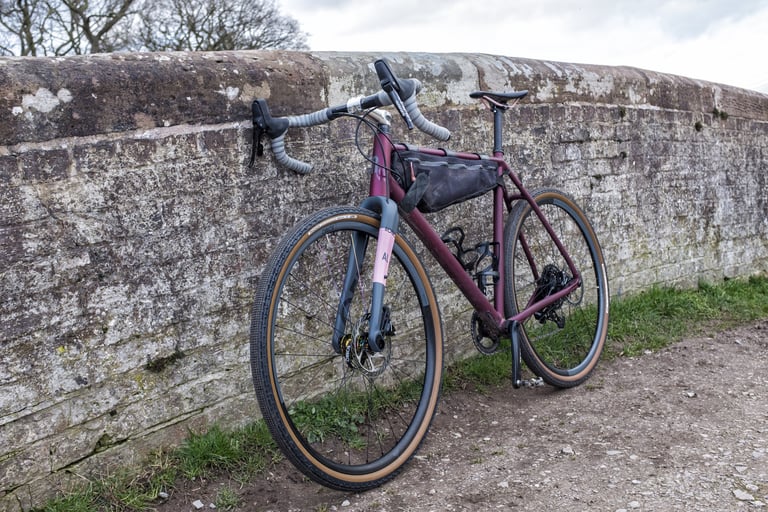Rondo Ruut AL in 650b form with tan-wall tyres, leaning on a stone wall beside a gravel path.