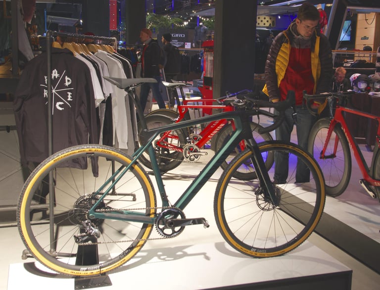 Canyon Grail CF SLX in green with tan-wall tyres on its plinth, with visitors and red bikes behind.