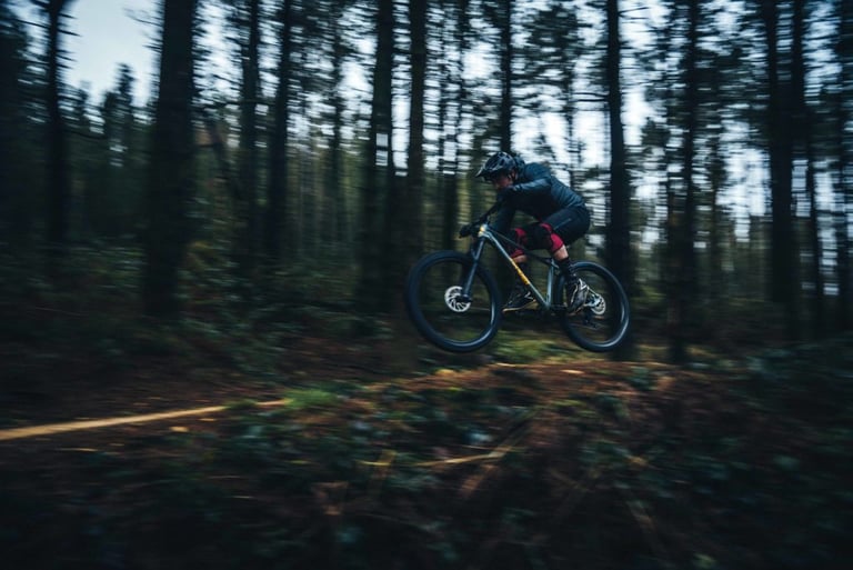 Rider airborne on the new Sonder Transmitter hardtail over a forest trail, trees blurred by motion.