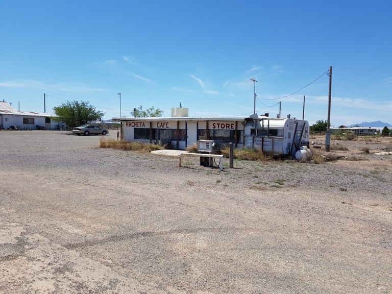 Hachita Cafe and Store, a weathered roadside building beside a trailer on a gravel forecourt in New Mexico.
