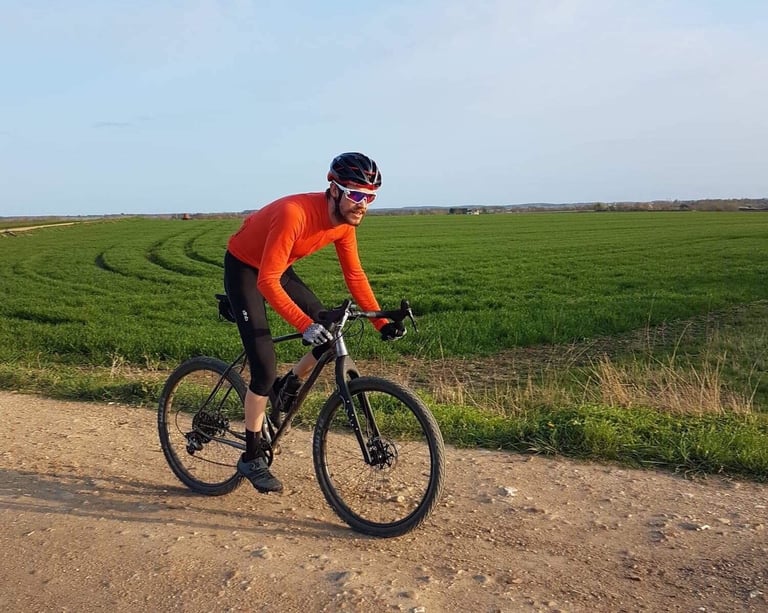 Josh Ibbett in an orange jersey rides the Mason ISO on a dry gravel track beside a green field.