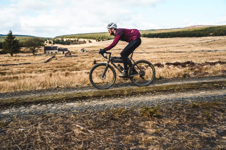 Rider on a gravel bike with a frame bag passes moorland farm buildings on the Dirty Reiver 2019 route.