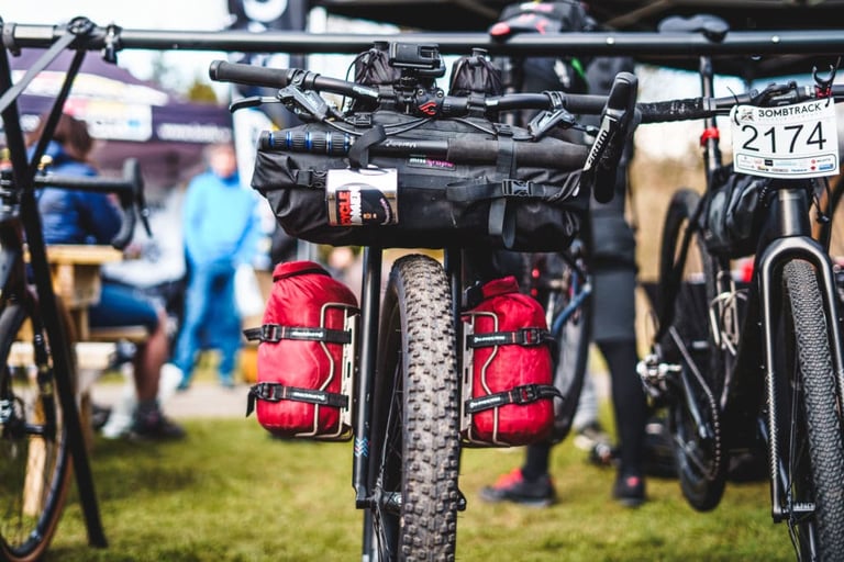 Gravel bike loaded with a handlebar roll and red fork-cage bags, racked beside others before Dirty Reiver 2019.
