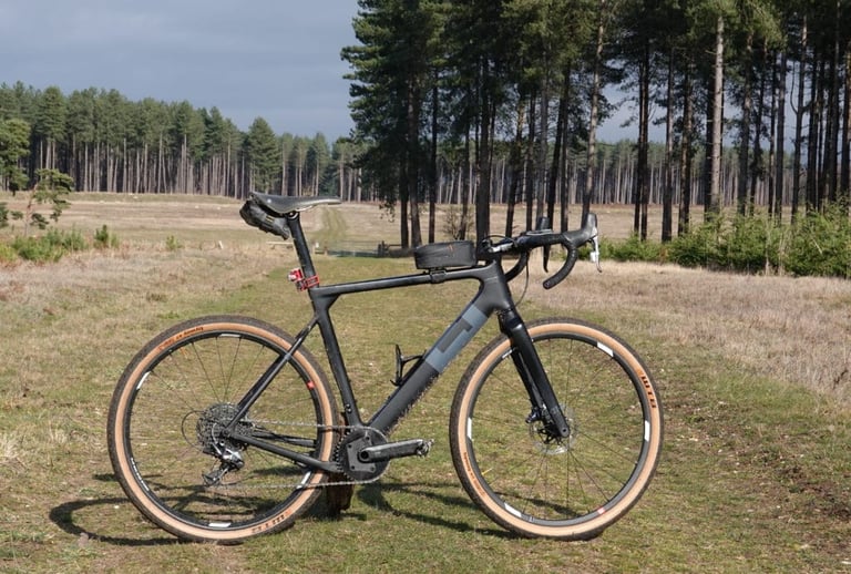 3T Exploro LTD from the drive side on heathland in front of pine forest, with a seat pack and top-tube bag.
