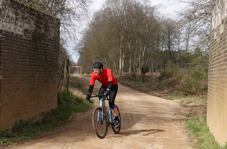 Rider on the Orbea Terra gravel bike heads along a wide gravel track between two brick walls.