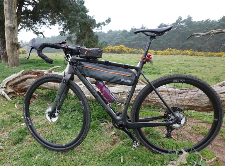 Side view of the carbon Bombtrack Hook EXT-C with SRAM Rival 1x, Ortlieb bags and Hunt wheels, on grass.