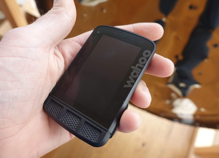 Hand holding a Wahoo ELEMNT ROAM, showing its size, flush Gorilla Glass screen and three rubber buttons below.