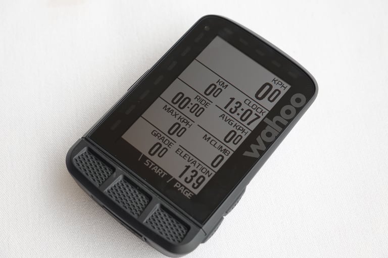 Wahoo ELEMNT ROAM on a white surface, its data page showing ride time, clock, speed, grade and elevation fields.