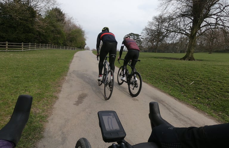 Wahoo ELEMNT ROAM on the handlebars as two riders ahead follow a narrow tarmac path through parkland.