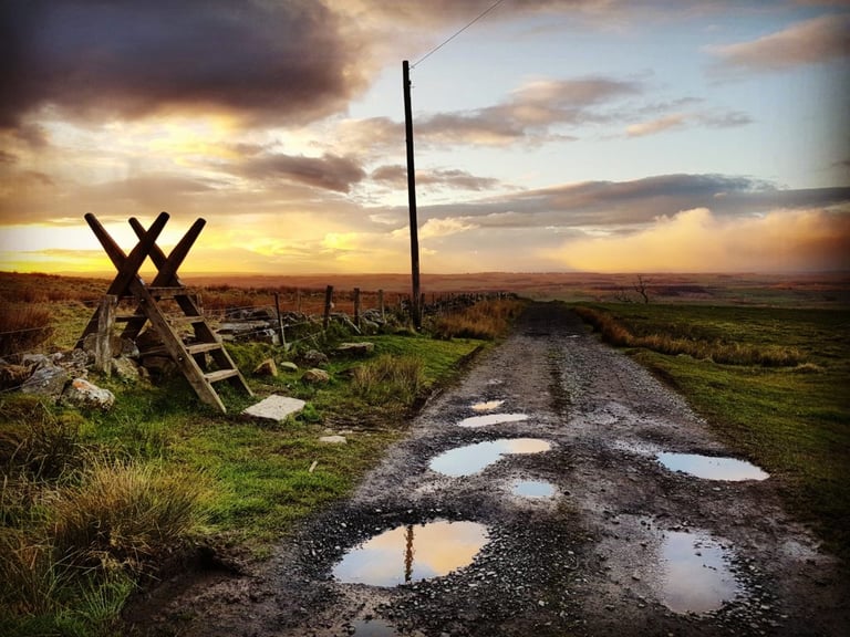 Puddled stony farm track at sunset beside a wooden stile, the real-world ground used to test tubeless sealant.