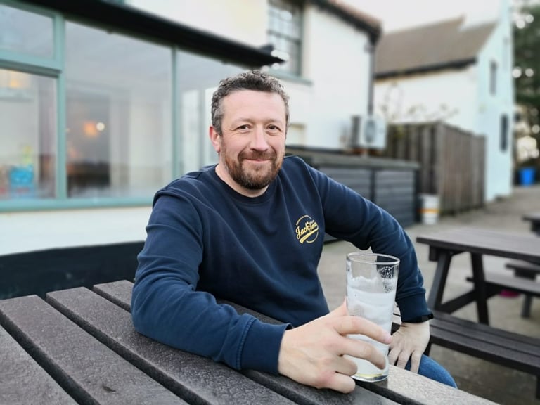 Fraser Barsby, founder of BiViBIKES, smiling at an outdoor picnic bench with a pint glass in hand.