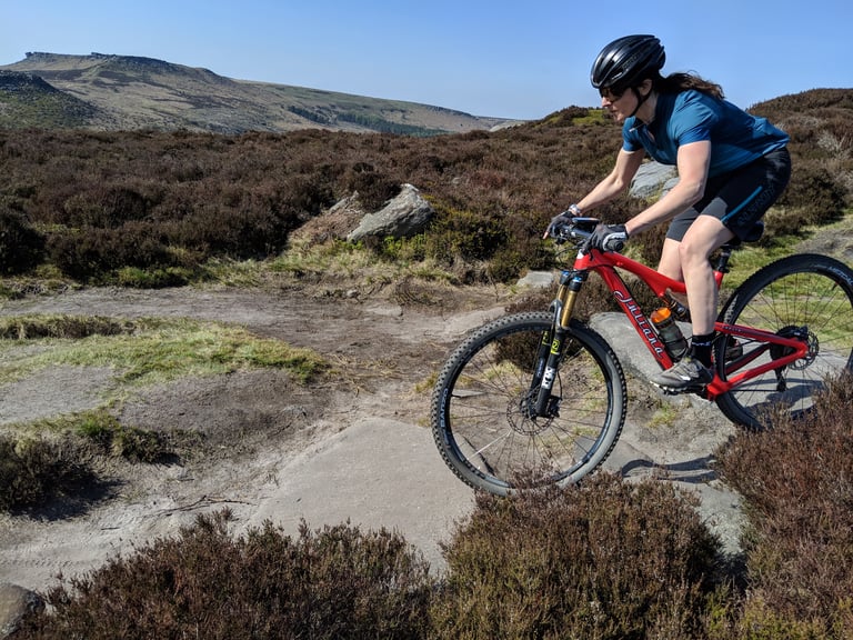 Rider in Alpkit Floe women's MTB shorts on a red full-suspension mountain bike on a moorland trail.