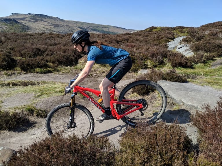 Side view of Alpkit Floe women's shorts in black with teal highlights while riding a rocky moorland path.