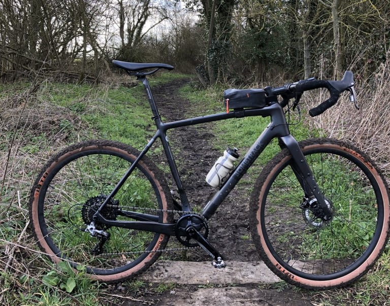 Bombtrack Hook EXT-C gravel bike with Ritchey WCS VentureMax bars, side-on on a muddy woodland track.