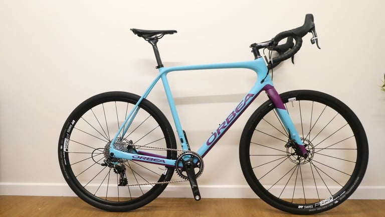 Orbea Terra M21-D 19 in light blue and purple with DT Swiss wheels, side view against a white wall.