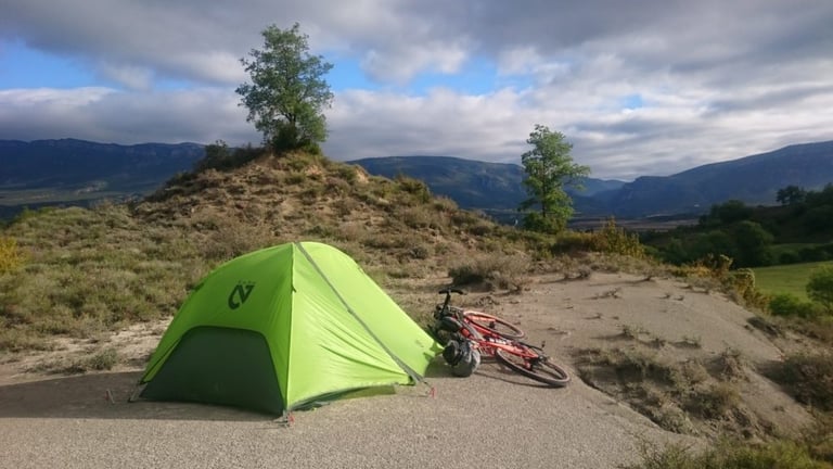 Bikepacking camp with a green tent pitched on a dry hilltop and a loaded red bike lying beside it.