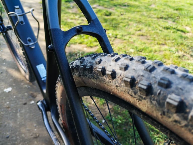 Mud-caked WTB Sendero 47 tyre in the rear triangle of the Bombtrack Hook EXT-C, showing the carbon frame's clearance.