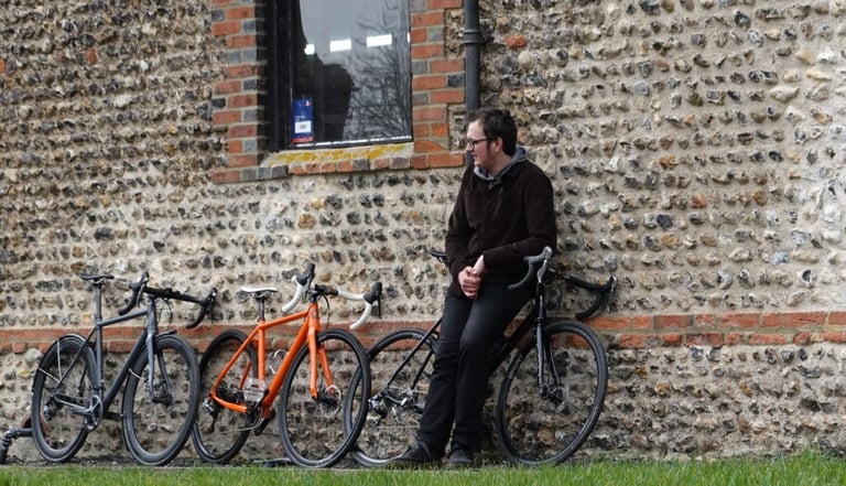 Three bikes lined up against the flint wall of the Mason barn, with a man leaning on one of them.