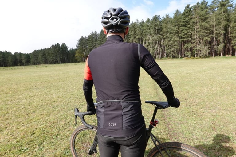 Back of the Gore C5 Gore-Tex Infinium jersey with rear pockets and reflective trim, rider beside a gravel bike.