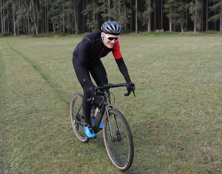 Rider on a gravel bike across grass in the Gore C5 Infinium jersey, showing its racer-cut fit.