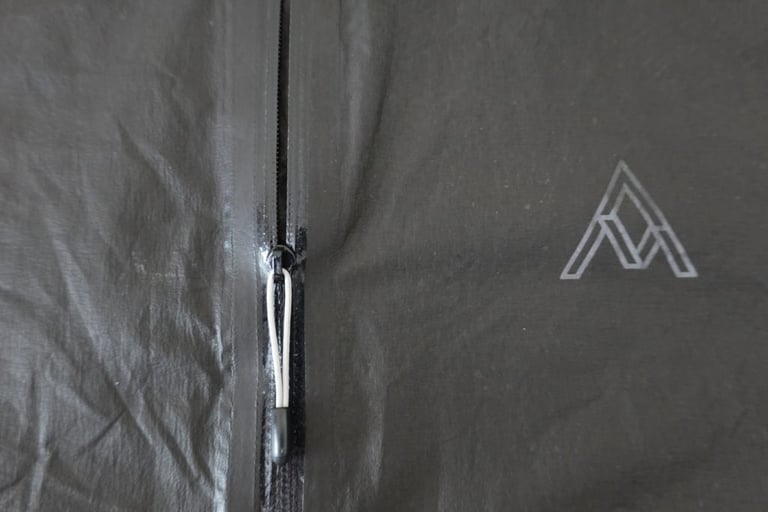 Close-up of the 7Mesh Oro jacket's water-resistant zip with its small cord toggle beside the chest logo.
