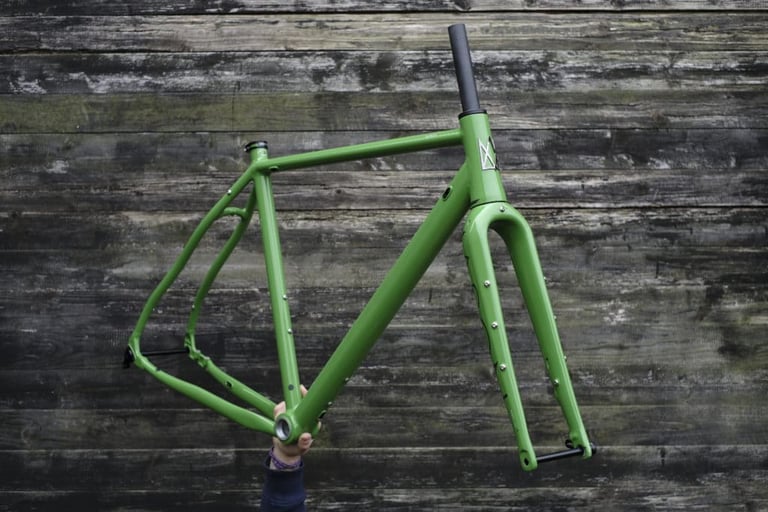 Green Mason Bokeh 2 frameset with Parallax2 fork, held up by hand against weathered wooden boards.