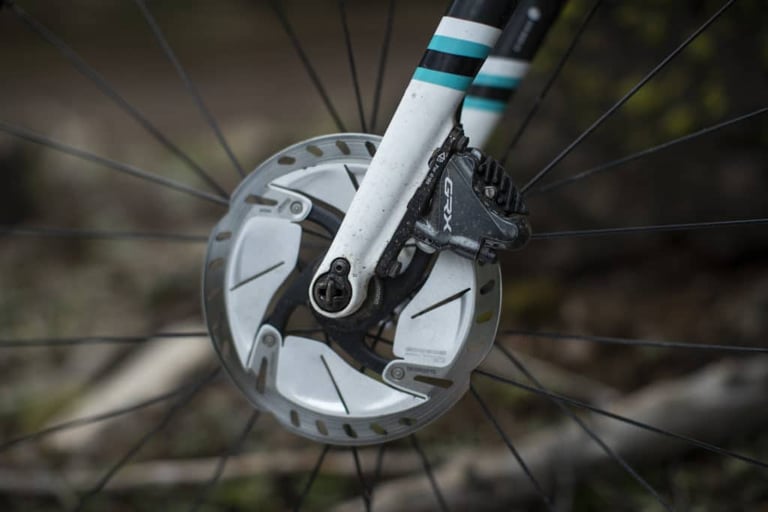 Shimano GRX brake caliper and finned rotor on the front fork of a white gravel bike.