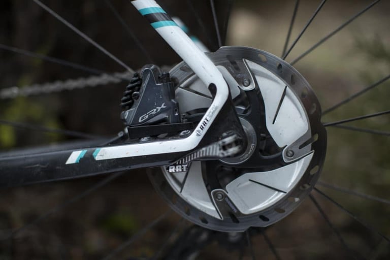 Shimano GRX flat-mount disc brake caliper and Ice Tech rotor on the rear of a white and black gravel bike frame.