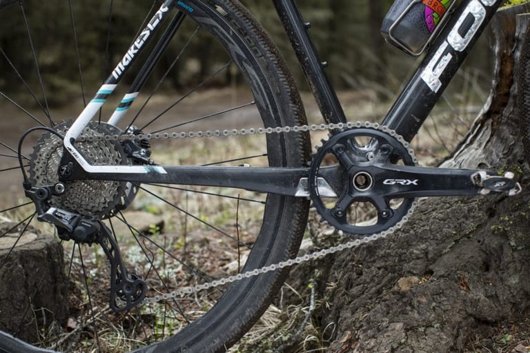 Single-ring Shimano GRX crankset and long-cage rear derailleur with wide-range cassette on a muddy gravel bike.