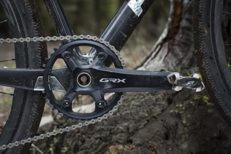 Shimano GRX single-chainring crankset with narrow-wide chainring and XT pedal on a muddy gravel bike.
