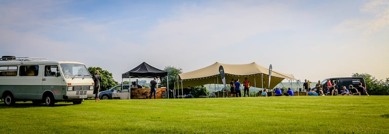 The Distance overnight basecamp on a grass field with a campervan, stretch tent and riders relaxing in the sun.