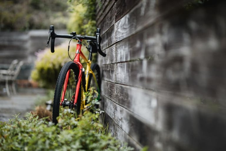 Red and yellow gravel bike on WTB Venture 700c x 40 tyres leaning against a weathered wooden wall.