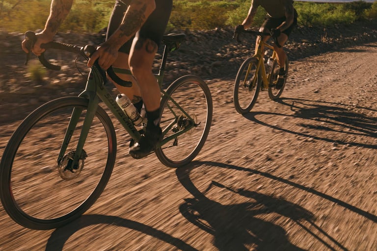 Close, low view of two Santa Cruz Stigmata riders speeding along a gravel track, shadows stretching across the dirt.