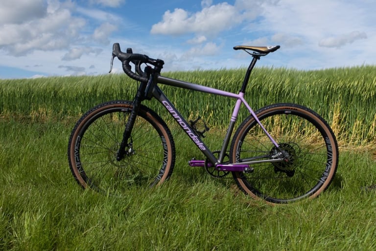 Cannondale Slate gravel bike with Lefty fork and purple cranks, side view in a grassy field.