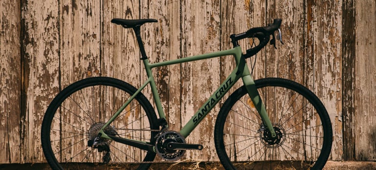Side view of the new Santa Cruz Stigmata in matt green against a weathered wooden wall, with disc brakes and 1x drivetrain.
