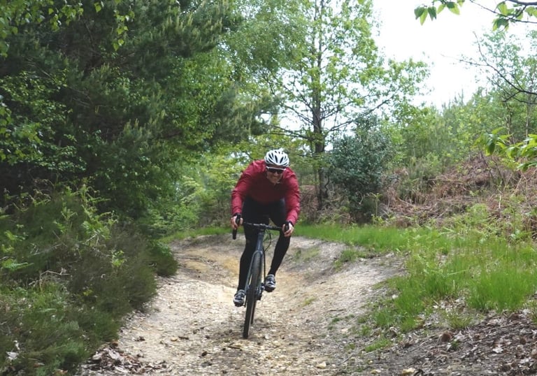 Grinning rider on a gravel bike descends a stony, rutted chute through scrub on the Swinley Gravel’duro route.