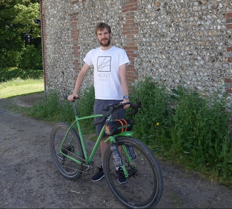 Josh Ibbett stands beside his green Mason InSearchOf gravel bike, fitted with a handlebar bag, before the Tour Divide.