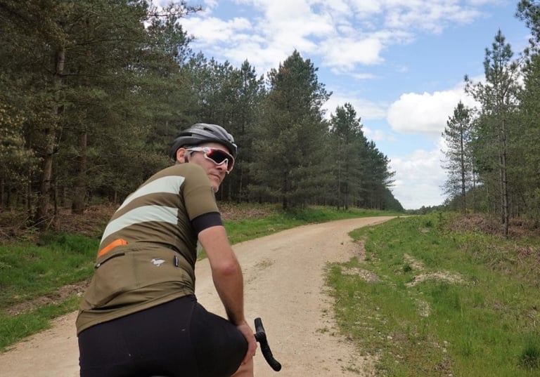 Rider in the green Blackmore Cadet jersey looks back over a shoulder on a gravel track through pines.