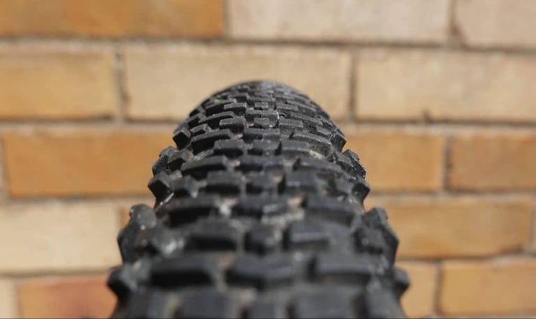 Close-up of the Donnelly EMP tread, with tightly packed centre blocks and wider side knobs, against a brick wall.