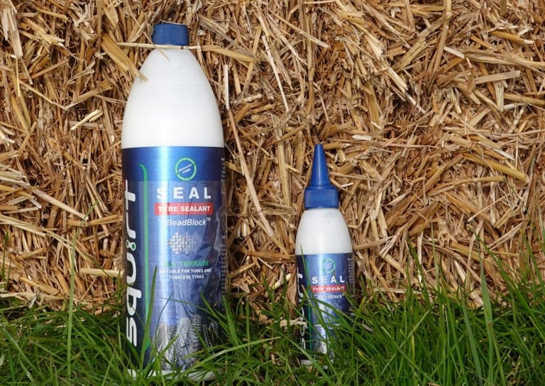 Squirt Seal tyre sealant in a 1 litre and a 150ml bottle standing against a straw bale.