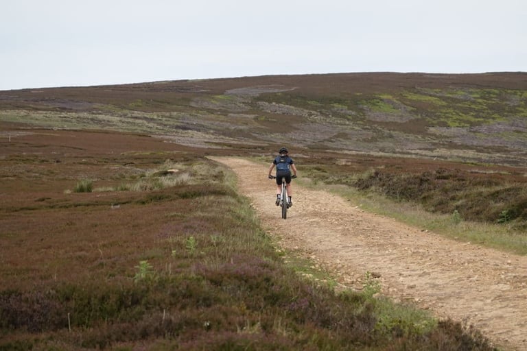 Rider on a gravel bike climbs a stony track across heather moorland while testing Squirt tyre sealant.