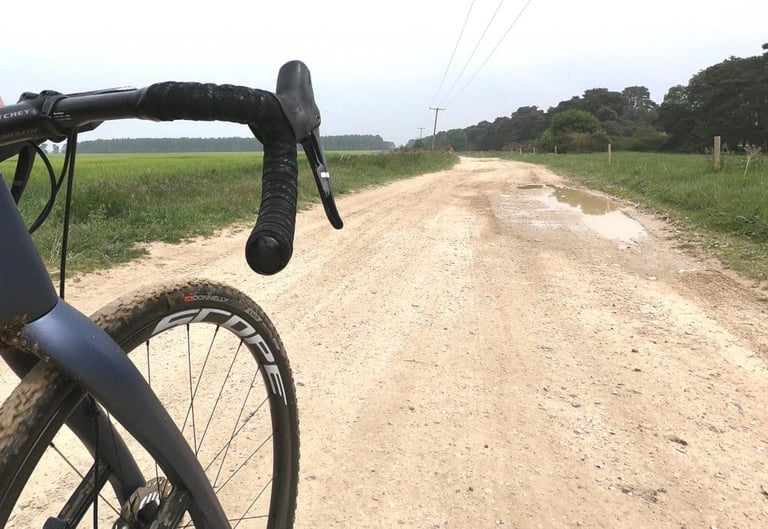 Donnelly EMP tyre on a Scope wheel, with a mud-flecked fork and handlebar, on a pale gravel road with a puddle.