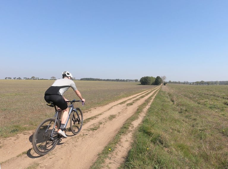 Rider in the 7Mesh Ashlu Merino Jersey on a gravel bike along a sandy double-track between open fields.