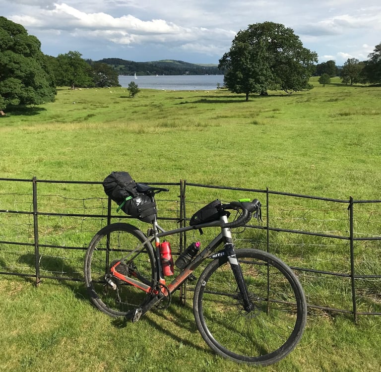 Marin Gestalt gravel bike with Miss Grape saddle and frame bags leaning on an iron fence above a Lake District lake.