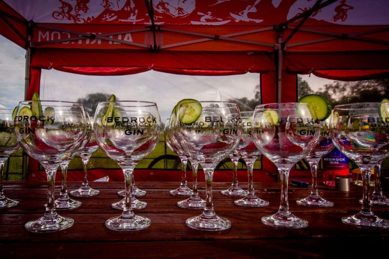 Rows of Bedrock Gin glasses with cucumber slices on a table under an Alpkit gazebo at The Distance overnight camp.