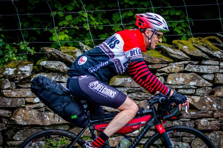 Close-up of a rider in a Belgians jersey with a saddle pack and frame bag riding past a mossy wall on The Distance.